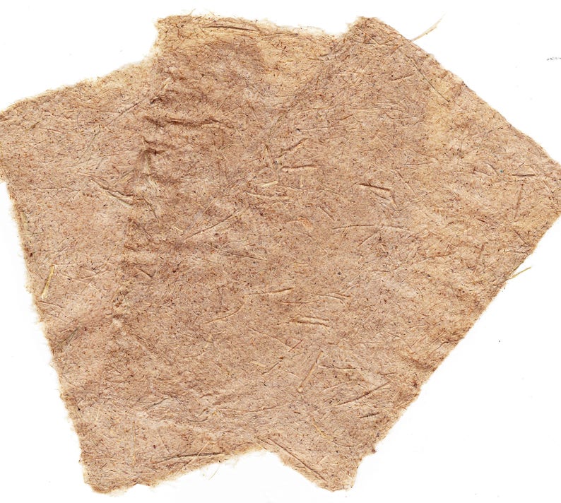 May include: Two pieces of handmade paper with a rough, textured surface. The paper is a light brown color with visible fibers and a slightly torn edge, set against a white background.