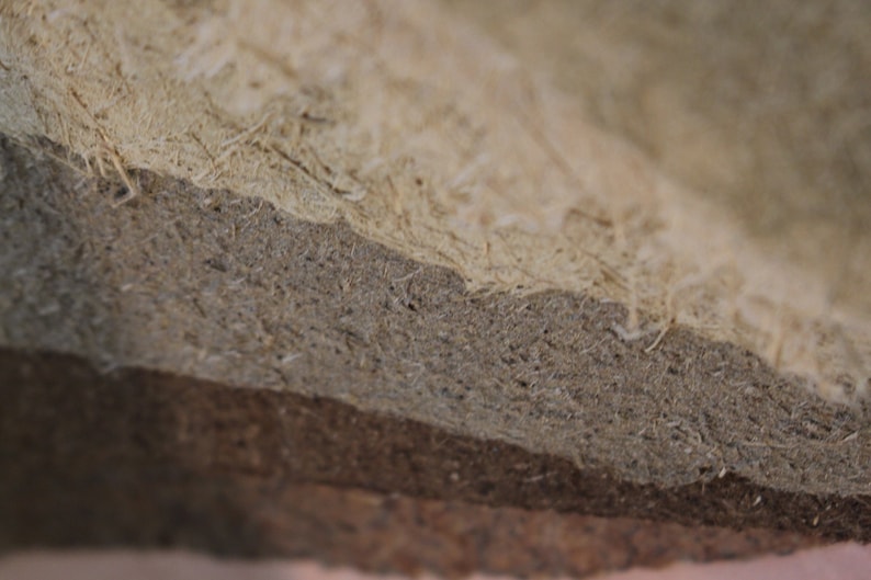 K&ouml;nnte beinhalten: Nahaufnahme eines geschichteten Materials mit nat&uuml;rlicher, strukturierter Optik. Die Schichten gehen von hellem Beige zu mittlerem Graubraun &uuml;ber, mit sichtbaren Fasern und einer rauen Oberfl&auml;che. Das Material scheint ein Verbundwerkstoff oder ein Naturprodukt zu sein.