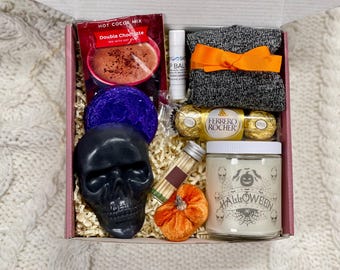 May include: A Halloween-themed gift box filled with various items, including a black skull, a pumpkin, a candle with the word "Halloween" on it, a package of hot cocoa mix, a pair of socks, and a box of chocolates.