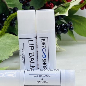 Op de afbeelding: Drie witte lippenbalsem tubes met zwarte en witte labels. De labels lezen "Lip Balm", "All Organic & Natural" en "1987 Shop".