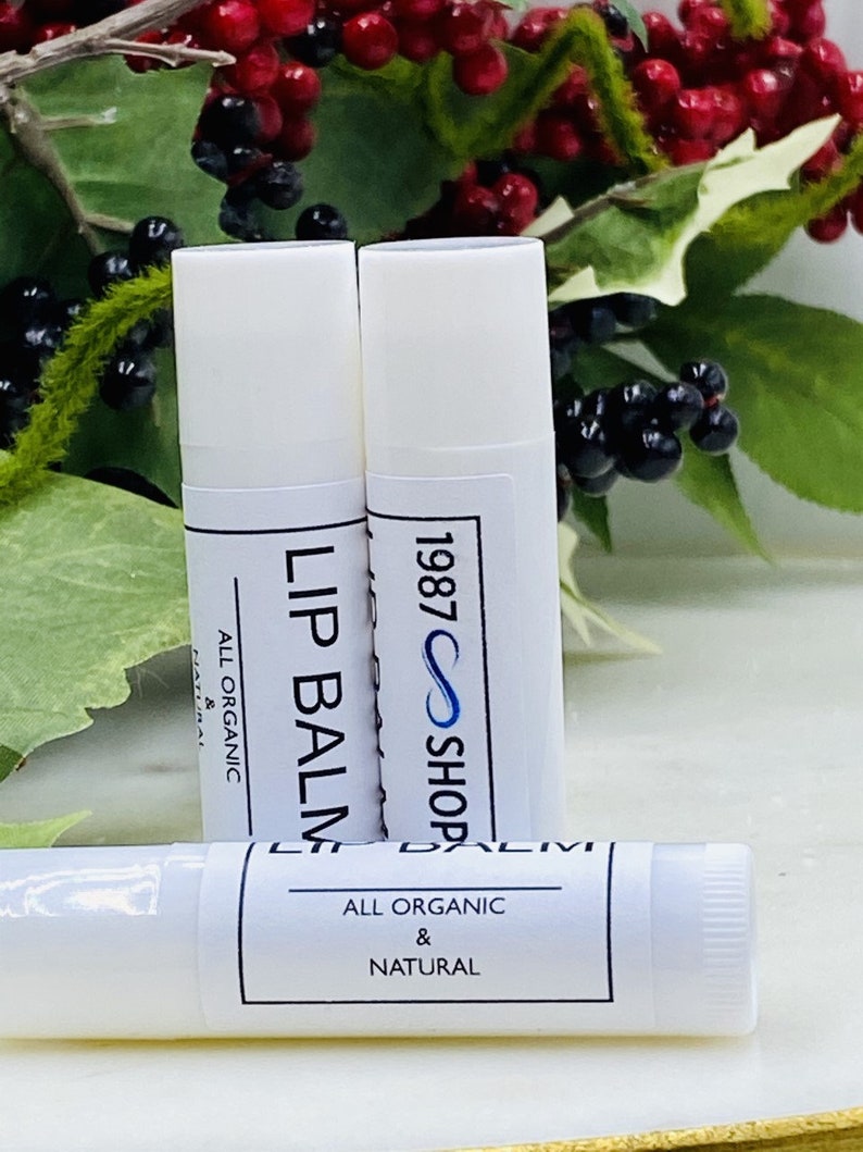 Op de afbeelding: Drie witte lippenbalsem tubes met zwarte en witte labels. De labels lezen "Lip Balm", "All Organic & Natural" en "1987 Shop".