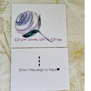 Puede incluir: Una tarjeta blanca con una ilustraci&oacute;n de acuarela de una rosa p&uacute;rpura y blanca. El texto "A Little Something For You To Enjoy" est&aacute; escrito en p&uacute;rpura debajo de la rosa. La parte posterior de la tarjeta tiene el texto "Your Message Is Here" escrito en negro con un s&iacute;mbolo de coraz&oacute;n negro.