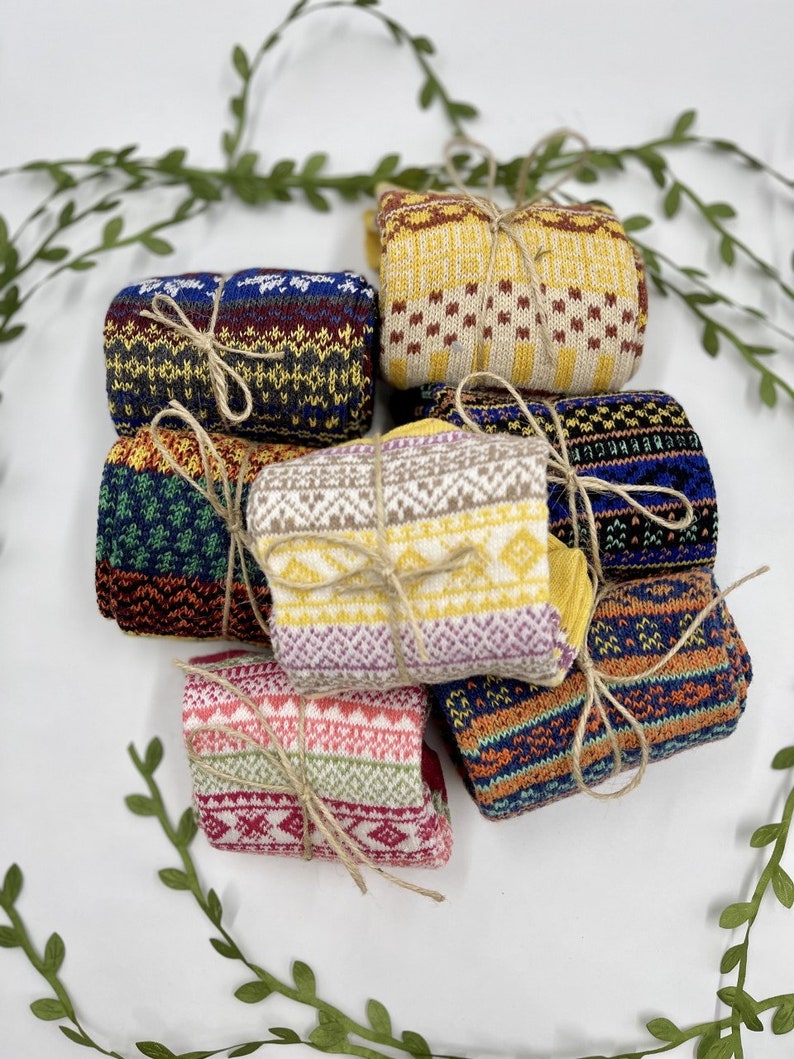 Op de afbeelding: Een set van zes paar kleurrijke gebreide sokken met verschillende patronen. De sokken zijn gevouwen en vastgebonden met touw.