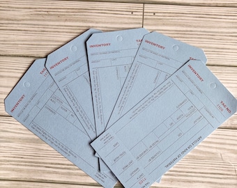 May include: A set of six blue inventory tags with red text. The tags have fields for article or kind of material, amount, unit, location, floor, section, comments, counted by, priced by, checked by, unit price, and total value. The tags are numbered 1109 and 1111.