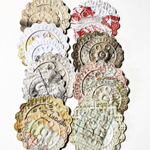 May include: A collection of vintage paper ephemera with a variety of designs, including maps, text, and floral patterns. The paper is aged and has a distressed look. The paper is in the shape of circles with scalloped edges.