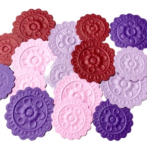 May include: Assortment of decorative paper embellishments in shades of purple, pink, and burgundy. Each embellishment features a raised floral design.