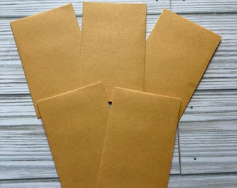 May include: Five brown paper envelopes stacked on top of each other. The envelopes are all the same size and shape.