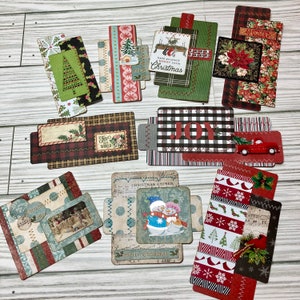 May include: A set of 10 Christmas themed paper crafting embellishments with various designs and patterns. The embellishments feature red, green, white, and black colors. Some of the embellishments have text, including "Joy", "Wonder", "Christmas Chimes", and "Merry Christmas Land".