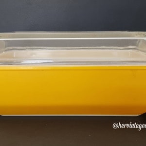 Könnte beinhalten: Eine gelbe Glasbackform mit einem durchsichtigen Glasdeckel. Die Form ist rechteckig und hat einen leicht abgerundeten Boden. Der Deckel hat an jeder Seite einen kleinen Griff.