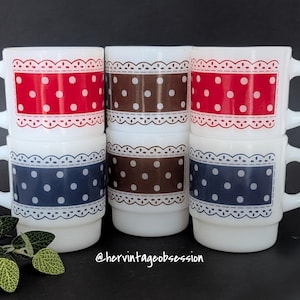 Puede incluir: Pila de tazas de cerámica blanca con un diseño retro. Cada taza presenta una banda de color con lunares blancos y un borde decorativo tipo encaje. Los colores incluyen rojo, marrón y azul marino. Las tazas tienen un diseño de asa clásico.