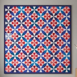 Op de afbeelding: Een vierkante quilt met een herhalend geometrisch patroon van rode, witte en blauwe windmolenvormen. Het ontwerp bestaat uit onderling verbonden cirkelvormige motieven met een donkerblauwe rand, met een levendig kleurenpalet.