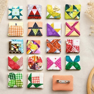 May include: A collection of nineteen square fabric patches featuring various colorful geometric quilt patterns, including stars, pinwheels, and checkered designs. One patch is shown from the back, revealing a silver metal pin backing.