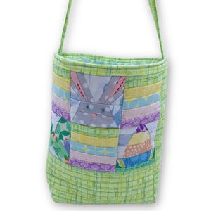 Puede incluir: Una bolsa de tela verde con diseño de patchwork y un diseño de conejo. La bolsa tiene una correa larga y es perfecta para llevar objetos pequeños.