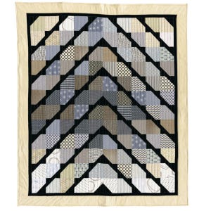 May include: A quilt with a geometric pattern of black, gray, and beige squares and rectangles. The quilt is made of different fabrics with various patterns, including stripes, polka dots, and floral designs.