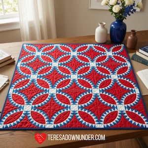 May include: A square quilt featuring a repeating pattern of red circular shapes with white and blue sawtooth edges, connected by small white squares. The quilt has a blue border and is laid flat, displaying intricate stitching throughout the fabric.