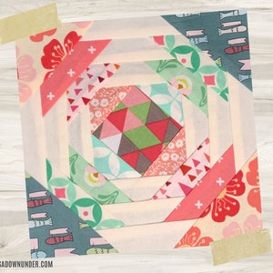 Può includere: Un blocco di trapunta patchwork colorato con un design geometrico. Il blocco è composto da vari tessuti in tonalità di rosa, rosso, verde, blu e bianco. Il blocco è circondato da un bordo bianco.
