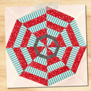 Könnte beinhalten: Ein roter und blauer Stoff-Patchworkblock mit geometrischem Muster. Der Block besteht aus Streifen und kleinen roten Punkten. Der Block ist von einem weißen Rand umgeben.