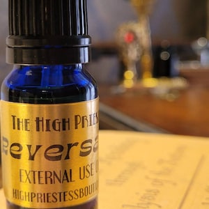 May include: A small blue glass bottle with a black cap. The bottle has a gold label that reads "The High Priestess Reversal External Use Only HighPriestessBoutique".