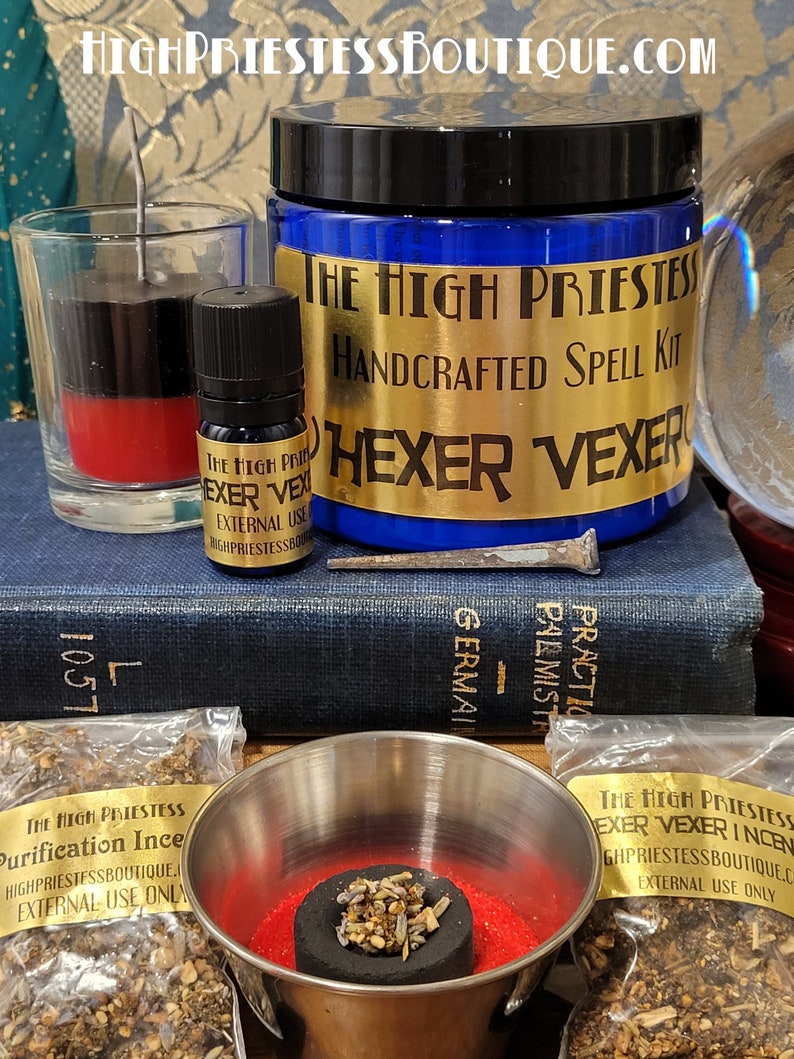 May include: A spell kit for hexing or vexing someone. The kit includes a blue glass jar with a gold label that reads "The High Priestess Handcrafted Spell Kit Hexer Vexer", a red and black candle, a small bottle of oil, a charcoal disc, incense, and a nail.