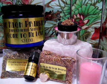 May include: A spell kit for love magic. The kit includes a blue jar with a gold label that reads "The High Priestess Handcrafted Spell Kit Come To Me Love $24.00", a small bottle of oil, a bag of incense, a pink candle, a pink heart-shaped crystal, and a metal incense burner with a black charcoal disc and incense on top.
