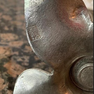May include: Close-up of a vintage metal object with a textured, silver-gray finish. The object has a curved, wing-like shape with a circular element on the right. The text "ZINN 0.50" is visible. The object appears to be a decorative or functional piece.