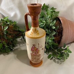 May include: A decorative ceramic vase with a handle, featuring a brown top and base, and a cream-colored body with a cracked glaze effect. The body is adorned with a painted scene of a figure in red and gold. The vase is approximately 8 inches tall.