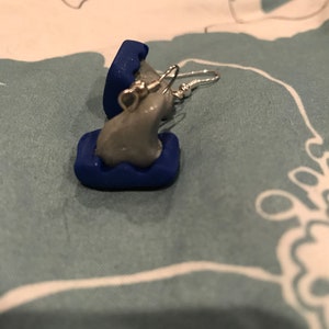 May include: A pair of gray and blue earrings with a silver hook. The earrings are shaped like a small cloud with a blue border.