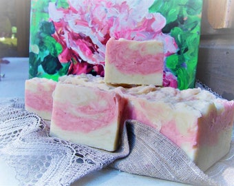 May include: Handmade soap bars with a pink and white swirl design. The soap is stacked on a lace doily and a gray cloth. A painting of pink flowers and green leaves is in the background.