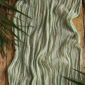 May include: A light green sheer fabric with a crinkled texture. The fabric is draped over a wooden surface.