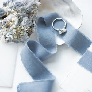 May include: A silver ring with two white pearls set in a seashell with a blue ribbon.