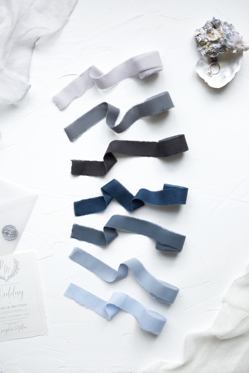 May include: A set of eight ribbon spools in various shades of blue, gray, and white. The ribbons are arranged in a gradient from light to dark.
