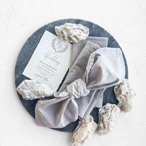 Pu&ograve; includere: Un invito di nozze con un design a conchiglia di ostrica grigia e bianca su un piatto di ardesia grigia. L'invito recita "The Wedding of Rachel & Matthew Saturday, September 1, 2019 at 4:00 PM Reception to follow"