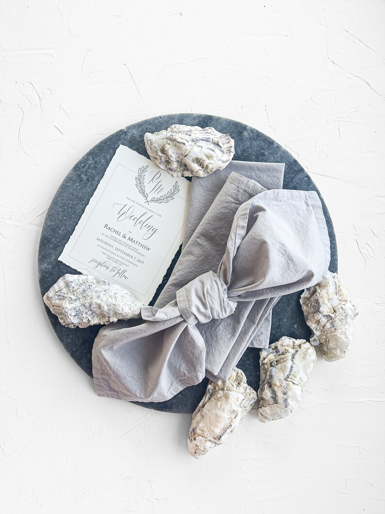 Pu&ograve; includere: Un invito di nozze con un design a conchiglia di ostrica grigia e bianca su un piatto di ardesia grigia. L'invito recita "The Wedding of Rachel & Matthew Saturday, September 1, 2019 at 4:00 PM Reception to follow"