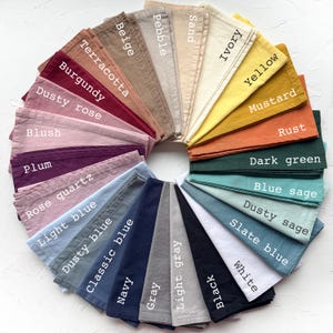 Peut inclure: Une présentation circulaire d'échantillons de tissu pliés dans diverses couleurs, dont le beige, le bordeaux et le marine. Chaque échantillon est étiqueté avec son nom de couleur, comme "Ivoire", "Moutarde" et "Noir". Les échantillons sont disposés en éventail.