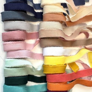 May include: A collection of colorful, frayed-edge ribbons in various shades, including blue, pink, yellow, and green. The ribbons are stacked and rolled, showcasing their textured appearance. Ideal for crafting and decorative projects.