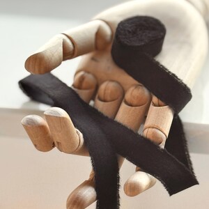 May include: Black velvet ribbon wrapped around a wooden hand. The ribbon is tied in a bow and the ends are frayed.