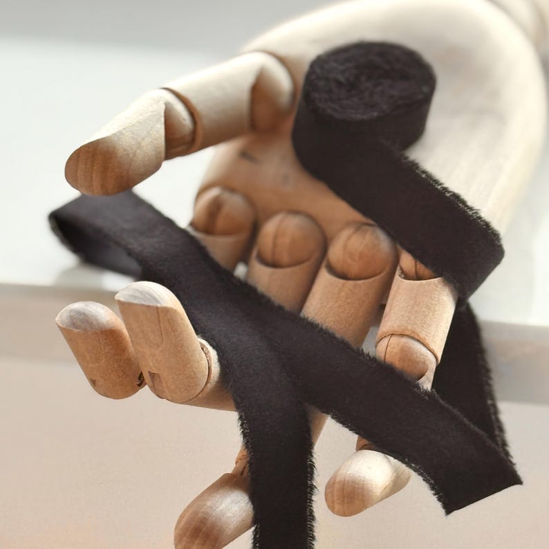 May include: Black velvet ribbon wrapped around a wooden hand. The ribbon is tied in a bow and the ends are frayed.