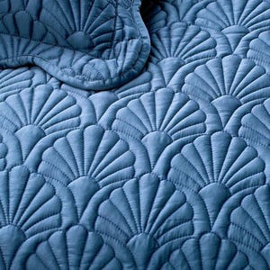 Puede incluir: Primer plano de un edredón acolchado azul con un diseño en forma de abanico. La tela tiene una textura suave y aterciopelada. Las costuras crean un diseño en relieve, agregando profundidad e interés visual a la ropa de cama.