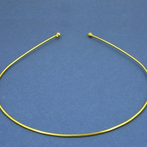 May include: A gold-coloured metal headband with rounded ends. The headband is thin and flexible.