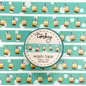 May include: A roll of turquoise washi tape with a repeating pattern of yellow and brown bubble tea cups with smiling faces. The tape is 15mm wide and 10m long. The text "tomkay washi tape 15mm x 10m www.tomkoy.com" is printed on the tape.