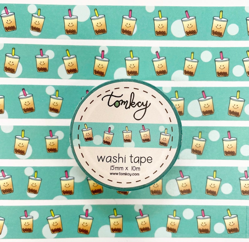 May include: A roll of turquoise washi tape with a repeating pattern of yellow and brown bubble tea cups with smiling faces. The tape is 15mm wide and 10m long. The text "tomkay washi tape 15mm x 10m www.tomkoy.com" is printed on the tape.