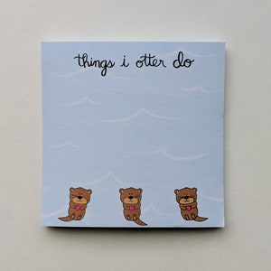 May include: A blue notepad with the text "things i otter do" in black cursive writing. Three brown otters with pink hearts are at the bottom of the notepad.
