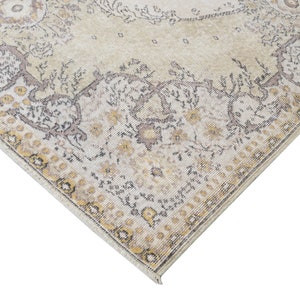 May include: Cream-colored area rug with an ornate, faded floral pattern. The rug features a central medallion design and a detailed border with yellow and gray accents. The distressed look adds a vintage aesthetic to the floor covering.