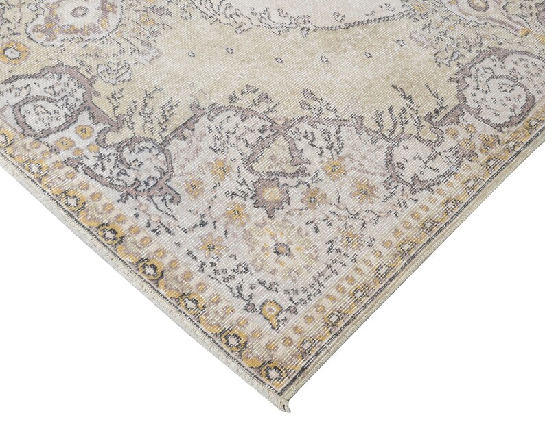 May include: Cream-colored area rug with an ornate, faded floral pattern. The rug features a central medallion design and a detailed border with yellow and gray accents. The distressed look adds a vintage aesthetic to the floor covering.