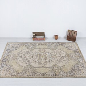 May include: A rectangular, beige and brown patterned rug with an ornate floral design. The rug is centered in the image, with a white background. The rug's dimensions are not visible.