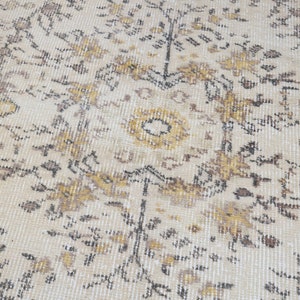 May include: Cream-colored area rug with an intricate floral pattern in shades of brown, gold, and black. The rug has a distressed, vintage look, with a soft, textured surface. The design features stylized flowers and leaves.