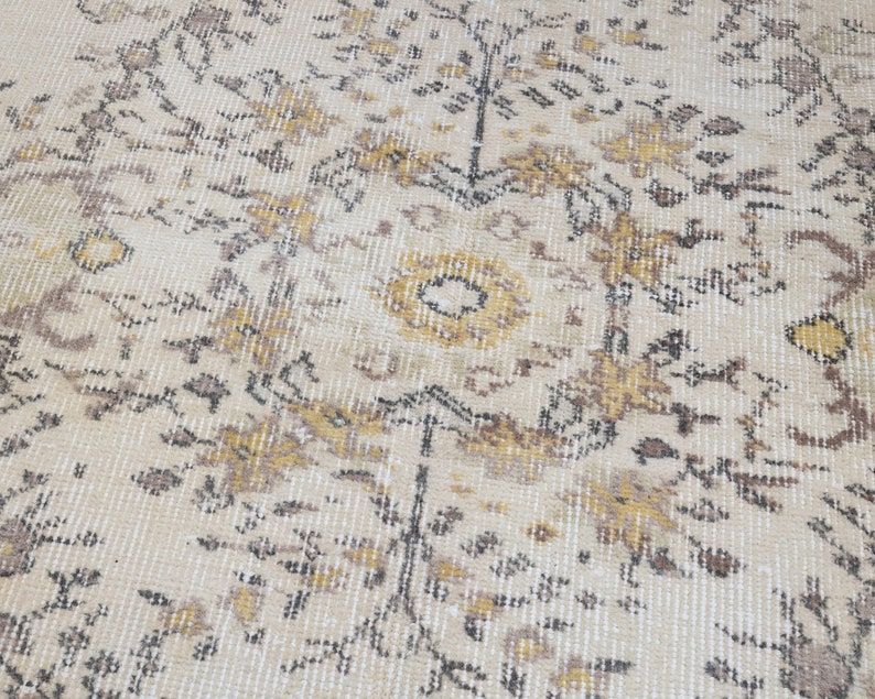 May include: Cream-colored area rug with an intricate floral pattern in shades of brown, gold, and black. The rug has a distressed, vintage look, with a soft, textured surface. The design features stylized flowers and leaves.