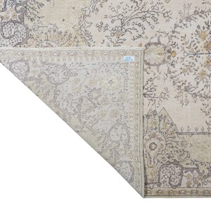 May include: Beige and gray area rug with an intricate floral pattern. The rug features a distressed, vintage look with a detailed border and corner designs. The rug is folded over, revealing the underside.