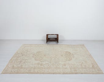 May include: A large, rectangular beige rug with an ornate floral pattern. The rug features a central medallion design and detailed borders. A small, dark wooden shelf sits in the background, adding depth to the scene.