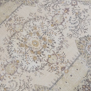 May include: Cream-colored area rug with an intricate floral pattern in shades of brown, gold, and black. The rug features a central medallion design and a border with geometric shapes. The rug's design is symmetrical and detailed.